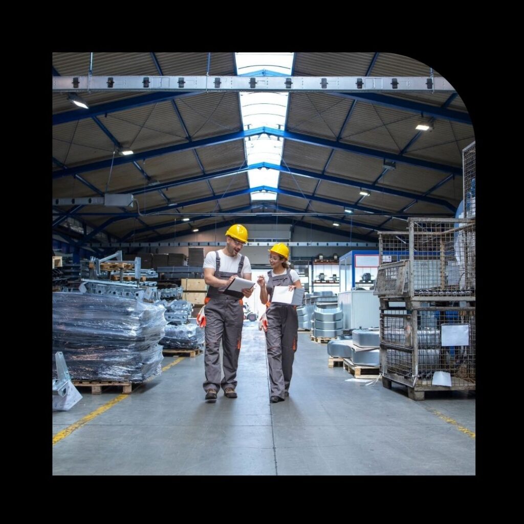 Profissionais da indústria com capacetes de segurança analisando documentos em galpão logístico com estoque de mercadorias — setor industrial e controle de operações